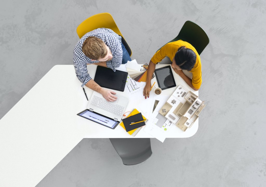 An aerial image of a man and woman sitting at a large desk table working