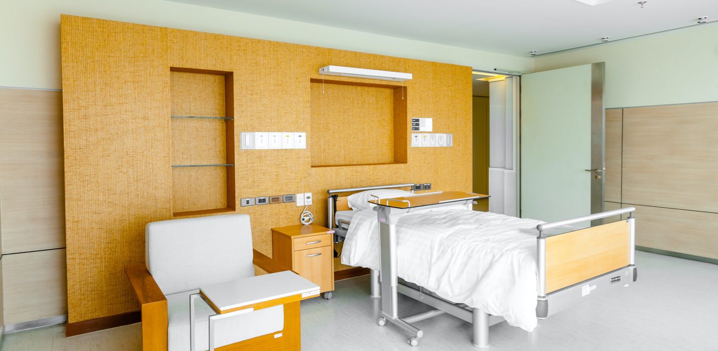 A hospital room with a bed and chair has walls made from Genesis Products laminate
