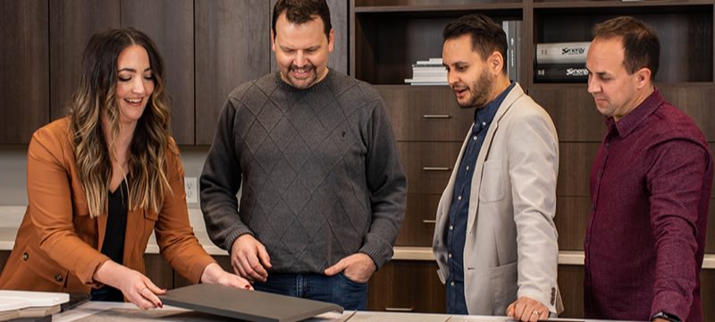 4 people stand in a showroom looking over laminate samples by Genesis Products