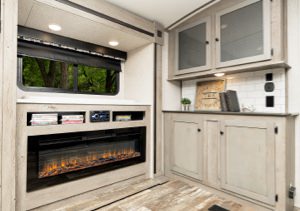 Interior of an RV with wooden floors, fireplace, cabinet, and window.