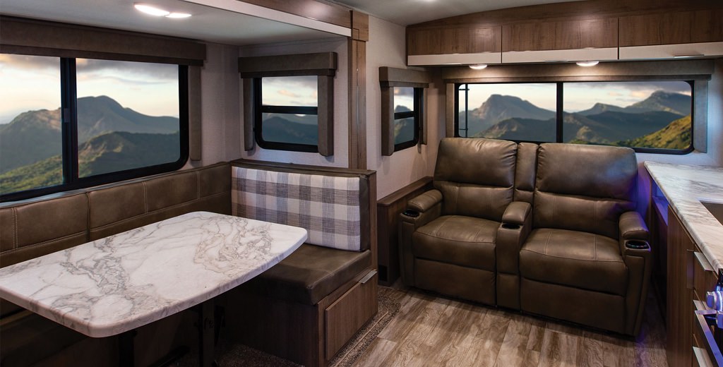 Inside of an RV with multiple windows, table, and seating options.