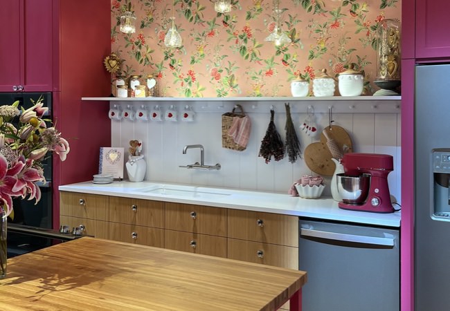 Kitchen with floral background, wooden and dark rose colored cabinets, and hanging lights.