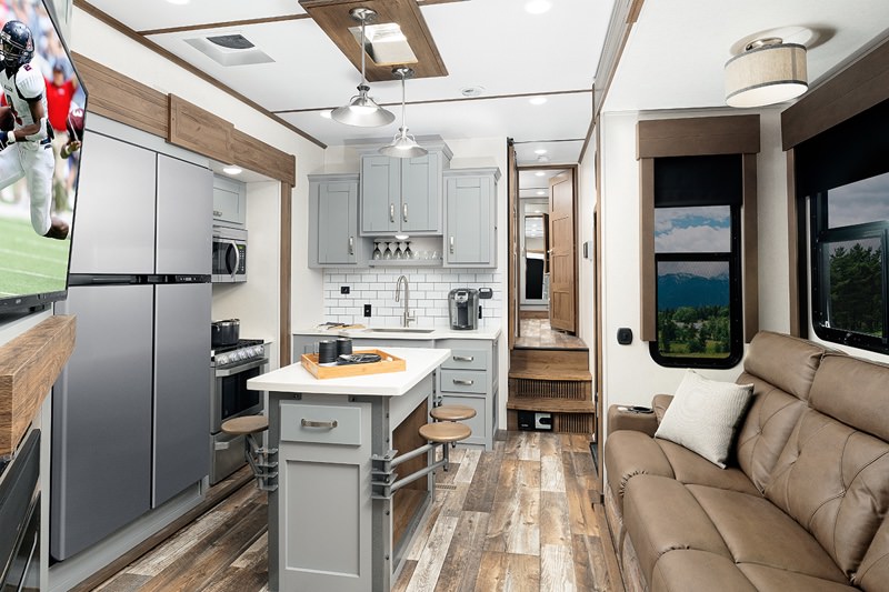 Interior of an RV with wooden floors, couch, tv, and kitchen.